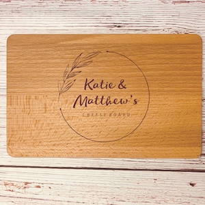May include: A wooden cheese board with a circle design engraved with the text "Katie & Matthew's Cheese Board" and a leafy branch design.