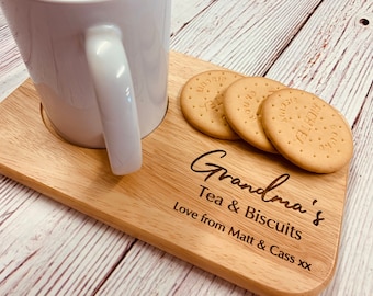 May include: A wooden tray with a white mug and four round biscuits. The tray is engraved with the text "Grandma's Tea & Biscuits Love from Matt & Cass xx".