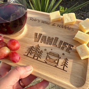 May include: A rectangular wooden serving board featuring the engraved text "Rob's Wine & Nibbles" and "VANLIFE" alongside a graphic of a camper van and pine trees. The board holds a glass of red wine, several red grapes, and cubes of cheese.