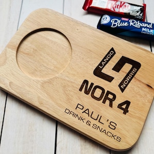 May include: Wooden serving tray with a round cutout for a cup or mug. The tray is engraved with the text "Lando Norris", "Nor 4", "Paul's", and "Drink & Snacks".