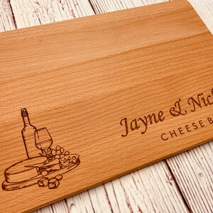 May include: A wooden cheese board with an engraved design of a wine bottle, glass, grapes, and cheese. The board is personalized with the text "Jayne & Nick's Cheese Board".