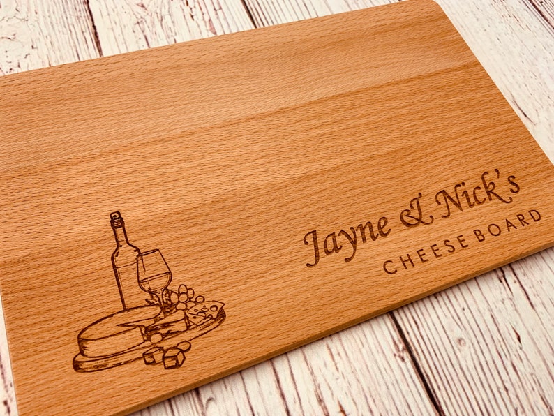 May include: A wooden cheese board with an engraved design of a wine bottle, glass, grapes, and cheese. The board is personalized with the text "Jayne & Nick's Cheese Board".