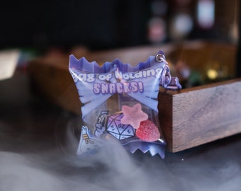 May include: A small purple and white bag of candy with the text "Bag of Holding Snacks!" printed on it. The bag is sitting on a wooden tray with a white, wispy cloud of smoke in the foreground.