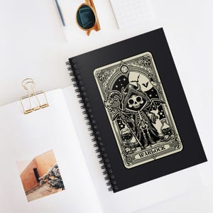 Puede incluir: Ilustración en blanco y negro de un personaje de warlock esqueleto en una libreta de espiral. El personaje lleva una túnica y sostiene un bastón. La libreta tiene una cubierta negra con un borde blanco.