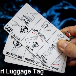 May include: Three-part luggage tag with hand gestures and phrases like "Go Up," "Go Down," and "Help." The tag includes a metal ring for attachment and the text "3 Part Luggage Tag."