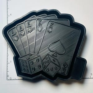 May include: Black cookie cutter featuring a poker hand of playing cards: Ace of Diamonds, Ace of Spades, Ace of Hearts, Ace of Clubs, King of Diamonds, King of Spades, and two dice. The cookie cutter is approximately 5 inches wide.