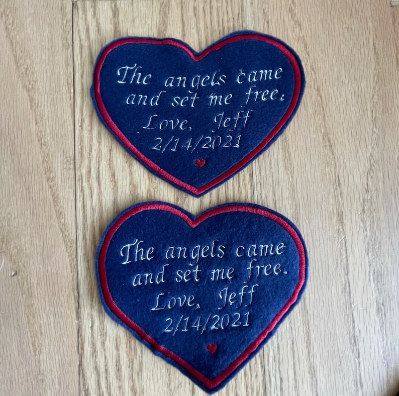 Może przedstawiać: Dwa sercowate łaty z niebieskiego filcu z czerwonymi szwami. Każda łata ma wyszyty białymi nićmi tekst "The angels came and set me free. Love, Jeff 2/14/2021".