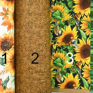 May include: Four fabric swatches with different patterns. The first swatch features a white background with sunflowers, leaves, and pumpkins. The second swatch is a brown fabric with a speckled pattern. The third swatch features a black background with sunflowers and birds. The fourth swatch is a green fabric with a striped pattern.