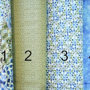 May include: Four fabric swatches with different patterns. The first swatch has a blue and green intricate pattern. The second swatch has a green and white geometric pattern. The third swatch has a white background with a blue and green geometric pattern. The fourth swatch has a blue and white watercolour pattern.