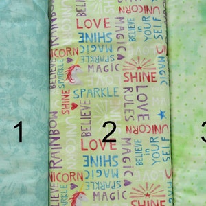 May include: Three different green fabric swatches with various patterns. The first swatch has a light green background with a subtle pattern of leaves and flowers. The second swatch has a light green background with a repeating pattern of words like "love", "shine", "magic", and "unicorn". The third swatch has a light green background with a repeating pattern of small white dots.