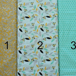 May include: Three fabric swatches with different patterns. The first swatch is a yellow fabric with a white floral pattern. The second swatch is a light blue fabric with a white floral pattern and yellow accents. The third swatch is a turquoise fabric with a white polka dot pattern. The swatches are labeled 1, 2, and 3.