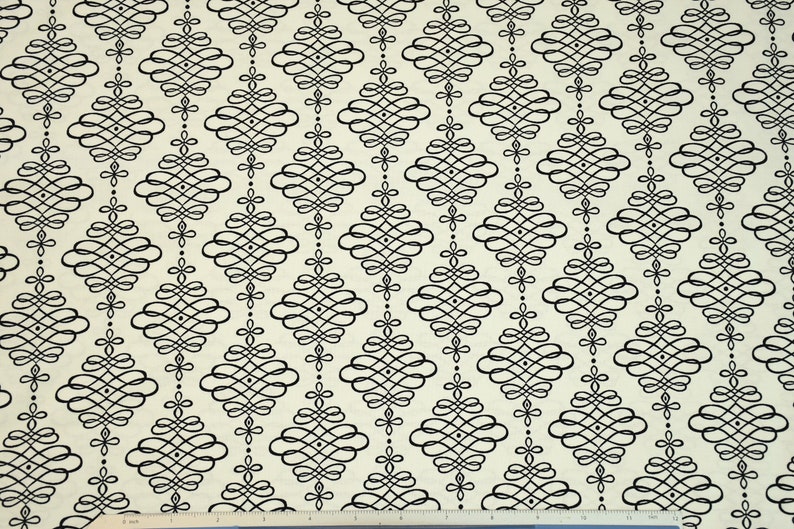 May include: A white fabric with a black repeating pattern of a stylized diamond shape with a swirl design. The fabric has a subtle texture.