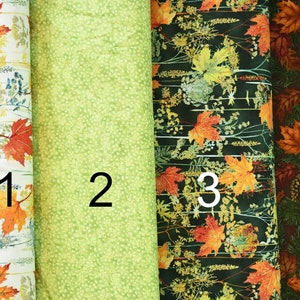 Może przedstawiać: Cztery próbki tkaniny z różnymi wzorami jesiennych liści. Pierwsza próbka jest biała z pomarańczowymi i żółtymi liśćmi, druga jest jasnozielona z kropkowanym wzorem, trzecia jest ciemnozielona z pomarańczowymi i żółtymi liśćmi, a czwarta jest ciemnobrązowa z igłami sosnowymi i pomarańczowymi i żółtymi liśćmi.