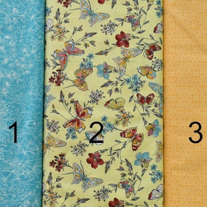 May include: Three fabric swatches, one light blue with a white floral pattern, one yellow with a butterfly and floral pattern, and one solid yellow with a subtle pattern.