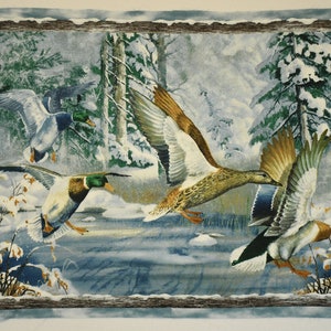 May include: A fabric panel depicting a winter scene with several ducks in flight over a snowy landscape. The ducks have brown, white, green, and blue plumage. The background includes snow-covered trees and a body of water.
