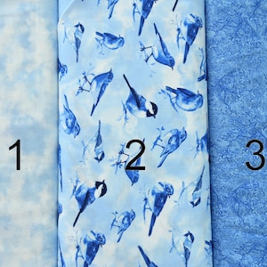 Peut inclure: Trois échantillons de tissu bleu différents. Le premier échantillon est bleu clair avec un motif de nuages blancs. Le deuxième échantillon est bleu clair avec un fond blanc et un motif d'oiseaux bleus. Le troisième échantillon est bleu foncé avec un motif blanc.