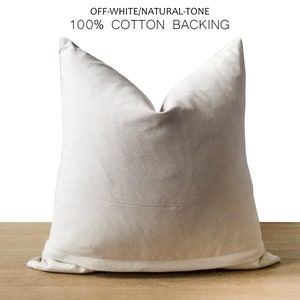 Pode incluir: Almofada de tom natural, branco-sujo, com forro 100% algod&atilde;o. A almofada quadrada &eacute; de cor neutra e assenta numa superf&iacute;cie de madeira. A almofada tem um design simples e minimalista, adequado para decora&ccedil;&atilde;o de interiores.