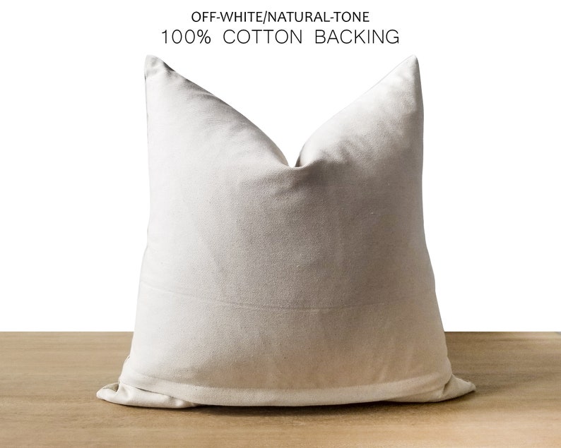 Pode incluir: Almofada de tom natural, branco-sujo, com forro 100% algod&atilde;o. A almofada quadrada &eacute; de cor neutra e assenta numa superf&iacute;cie de madeira. A almofada tem um design simples e minimalista, adequado para decora&ccedil;&atilde;o de interiores.