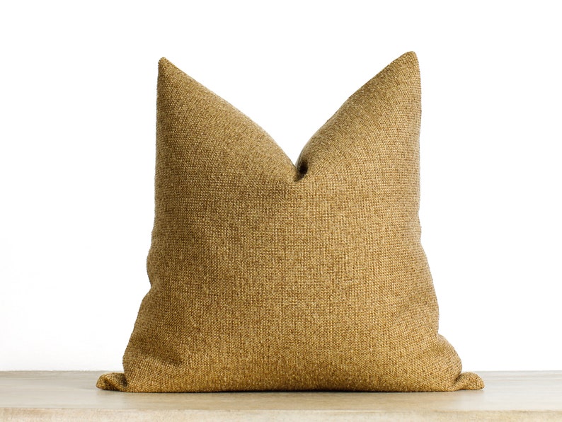 May include: A large, textured decorative pillow in a warm, golden-brown hue. The pillow has a classic shape with a pointed top and a soft, inviting appearance. The fabric appears to be woven, adding depth and visual interest to the design.
