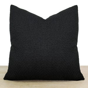 May include: A black square pillow with a textured fabric. The pillow is made of a soft, comfortable material.