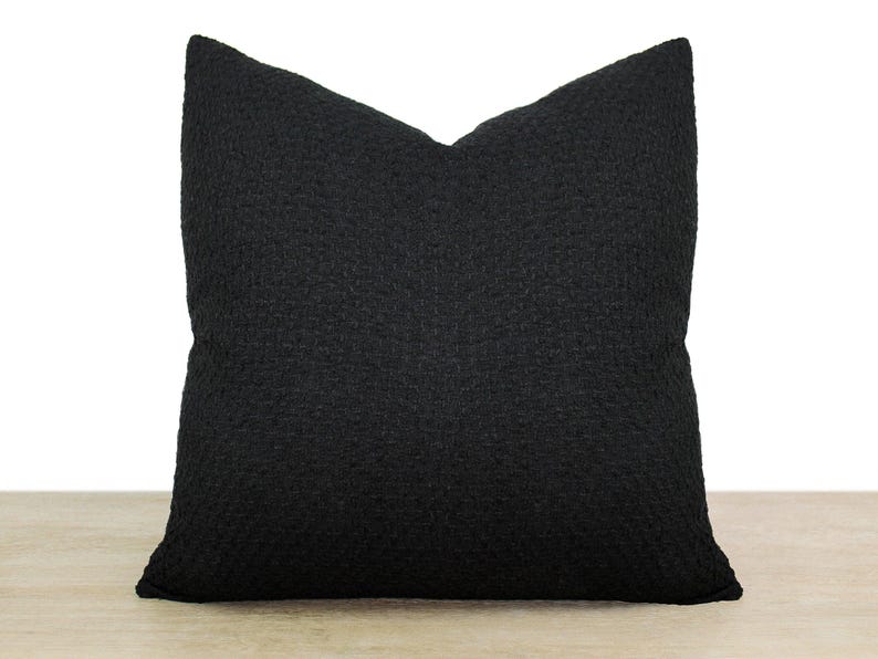 May include: A black square pillow with a textured fabric. The pillow is made of a soft, comfortable material.