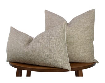 May include: Two square throw pillows featuring a textured, light beige fabric with a subtle woven pattern. The pillows are arranged with one positioned slightly in front of the other, both displaying a clean, structured shape with visible seams.