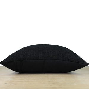 May include: A black square pillow with a textured woven fabric cover. The pillow has a solid black back.