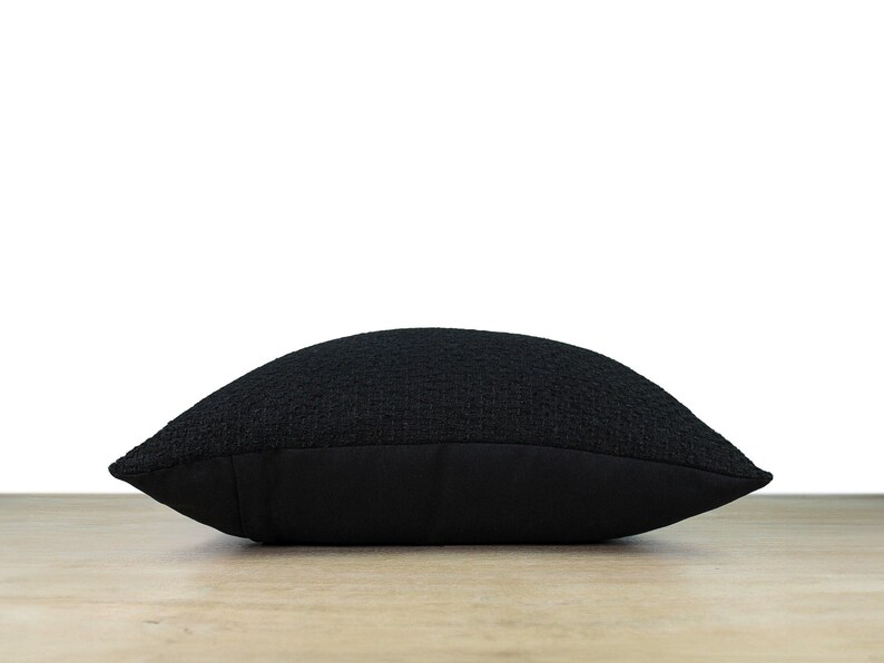 May include: A black square pillow with a textured woven fabric cover. The pillow has a solid black back.