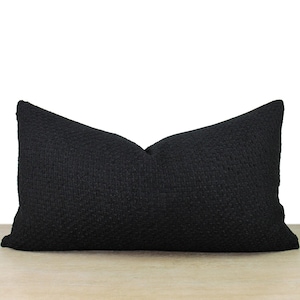 May include: A black pillow with a textured fabric. The pillow is rectangular and has a simple design.