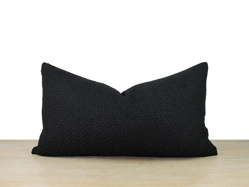 May include: A black pillow with a textured fabric. The pillow is rectangular and has a simple design.