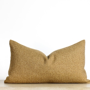 May include: A rectangular decorative pillow in a warm, golden-brown color. The pillow has a textured, woven appearance and is placed against a white background. The pillow is approximately 24 inches long.