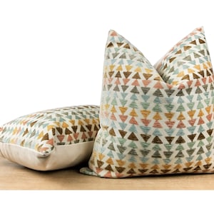 May include: Two decorative throw pillows with a geometric pattern of brown, green, blue, pink, and yellow triangles on a white background.