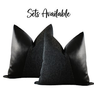 May include: Two decorative throw pillows. The pillows have a black leather-like material on the sides and a textured dark gray fabric in the center. The text "Sets Available" is written in cursive at the top.