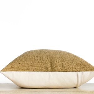 May include: A decorative pillow with a two-tone design. The top half features a textured, golden-brown fabric, while the bottom half is a smooth, off-white material. The pillow is rectangular and rests on a light-colored surface.