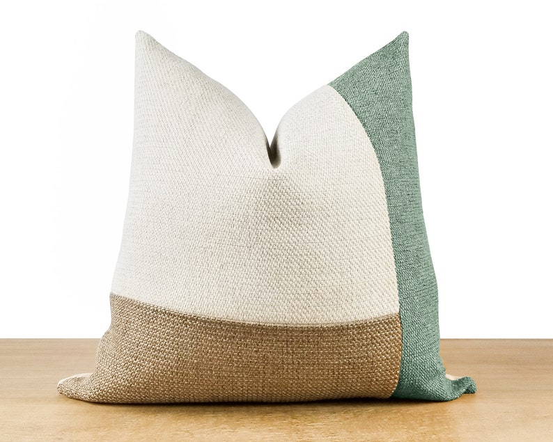 Pode incluir: Uma almofada decorativa com um design de blocos de cores. A almofada apresenta uma parte superior creme, uma parte inferior castanha e um painel lateral verde. A almofada &eacute; feita de um tecido texturizado e &eacute; projetada para decora&ccedil;&atilde;o de casa.