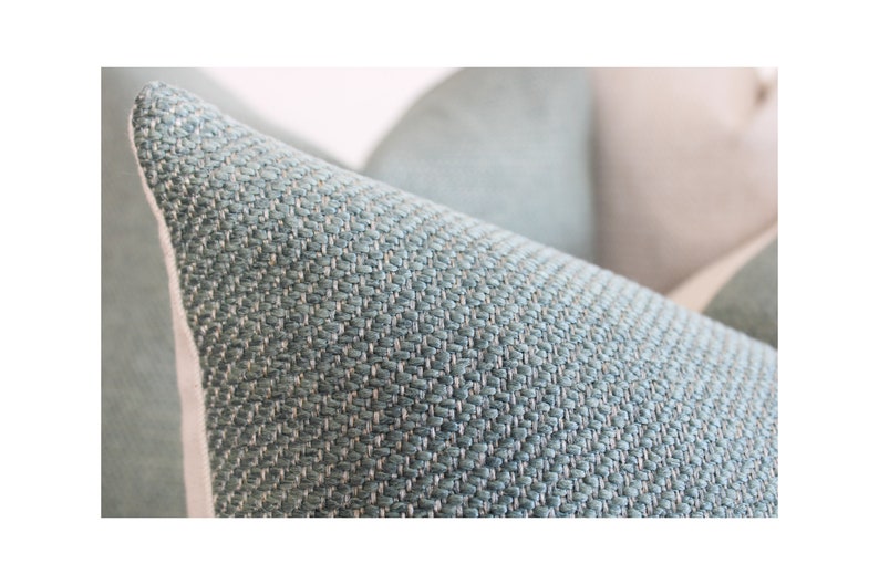 May include: Close-up of a teal-colored pillow with a textured weave. The pillow has a light-colored border and a soft, inviting appearance. The fabric has a subtle pattern, suggesting a comfortable home decor item.