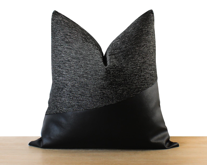 May include: A decorative throw pillow with a two-tone design. The top half features a textured gray fabric, while the bottom half is a smooth black material. The pillow is designed for home decor.