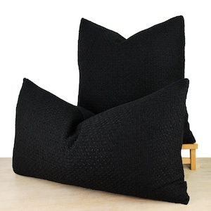 May include: Two black decorative throw pillows with a textured fabric. The pillows are stacked on top of each other.