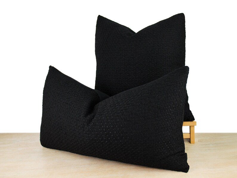 May include: Two black decorative throw pillows with a textured fabric. The pillows are stacked on top of each other.