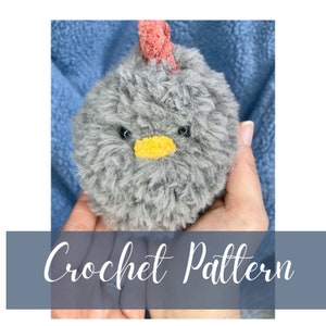 May include: A grey crocheted chick with a pink comb and yellow beak. The chick is being held in someone's hands. Crochet Pattern.