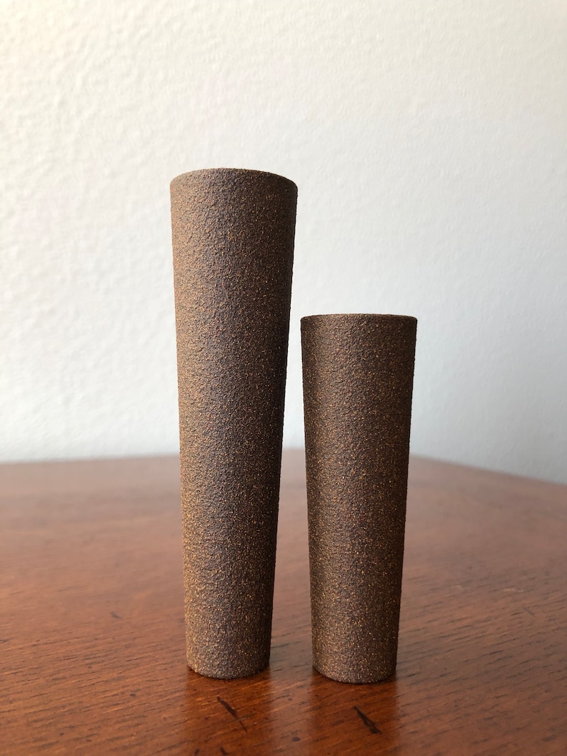 Puede incluir: Dos jarrones de cer&aacute;mica marr&oacute;n con una superficie texturizada. El jarr&oacute;n m&aacute;s alto est&aacute; a la izquierda y el m&aacute;s bajo a la derecha.