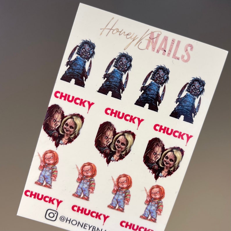 May include: A white sheet of nail decals featuring illustrations of the character Chucky. The sheet includes multiple images of the doll holding knives, heart-shaped portraits of Chucky and Tiffany, and the text CHUCKY and Honey NAILS.
