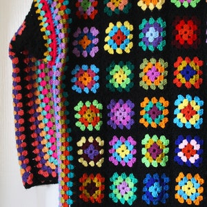Puede incluir: Una chaqueta de ganchillo colorida con fondo negro y una variedad de cuadrados de colores brillantes. La chaqueta est&aacute; hecha con un punto de granny square y tiene una silueta larga y fluida.