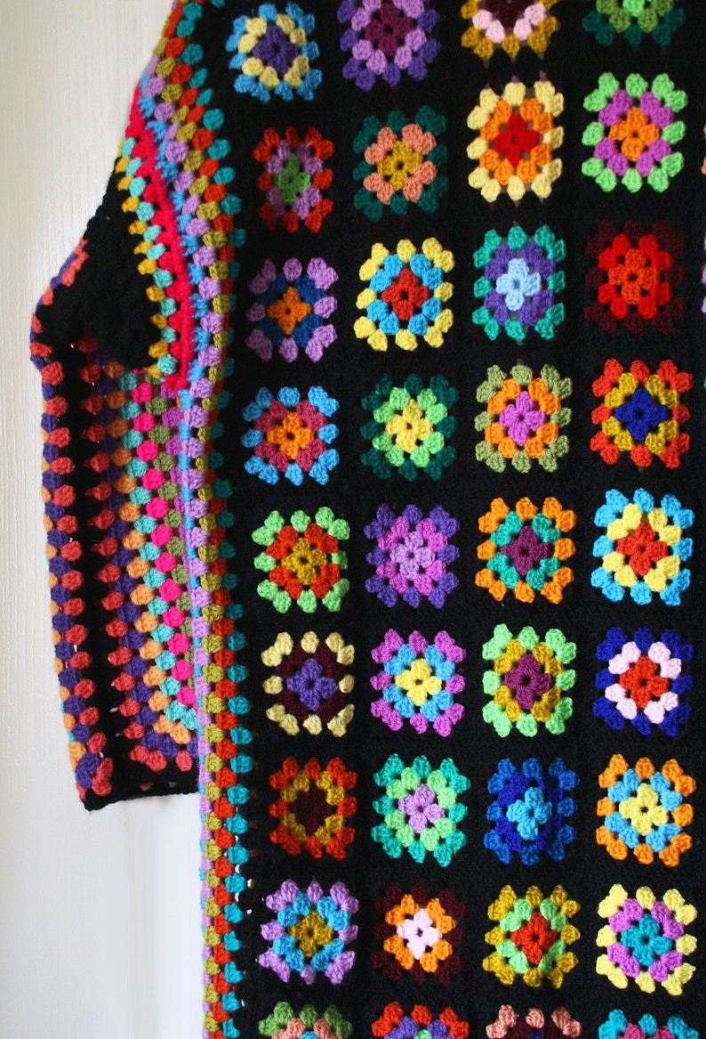 Puede incluir: Una chaqueta de ganchillo colorida con fondo negro y una variedad de cuadrados de colores brillantes. La chaqueta est&aacute; hecha con un punto de granny square y tiene una silueta larga y fluida.
