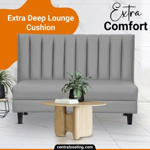 May include: A gray, tufted, extra deep lounge cushion with a wooden table and a potted plant in front of it. The text "Extra Deep Lounge Cushion" and "Extra Comfort" is visible in the image.