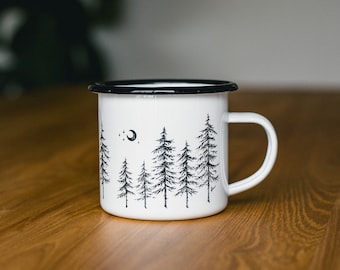 May include: White enamel mug with a black rim and handle. The mug has a black and white illustration of a crescent moon and a row of pine trees.