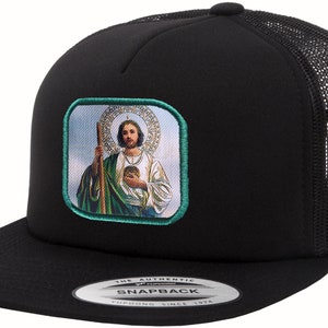 May include: Black trucker hat with a mesh back and a flat brim. The front features a square patch with an image of a religious figure holding a staff and a medallion. The hat has a snapback closure.