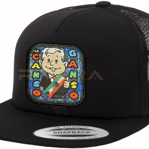 May include: Black trucker hat with a square patch featuring a cartoon character holding a Mexican flag. The patch has the word "CANSO" around the character. The hat has a mesh back and a snapback closure.