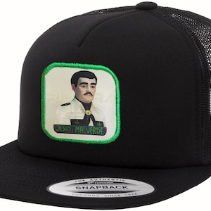 May include: Black trucker hat with a flat brim and mesh back. The front features a patch with an image of a man and the text "JESUS. MALVERDE" in green. The hat has a snapback closure.