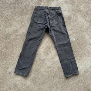 May include: A pair of faded black denim jeans, viewed from the back. The jeans feature classic five-pocket styling, with the Levi's brand label visible on the back pocket. The jeans are slightly worn, with a straight leg cut.